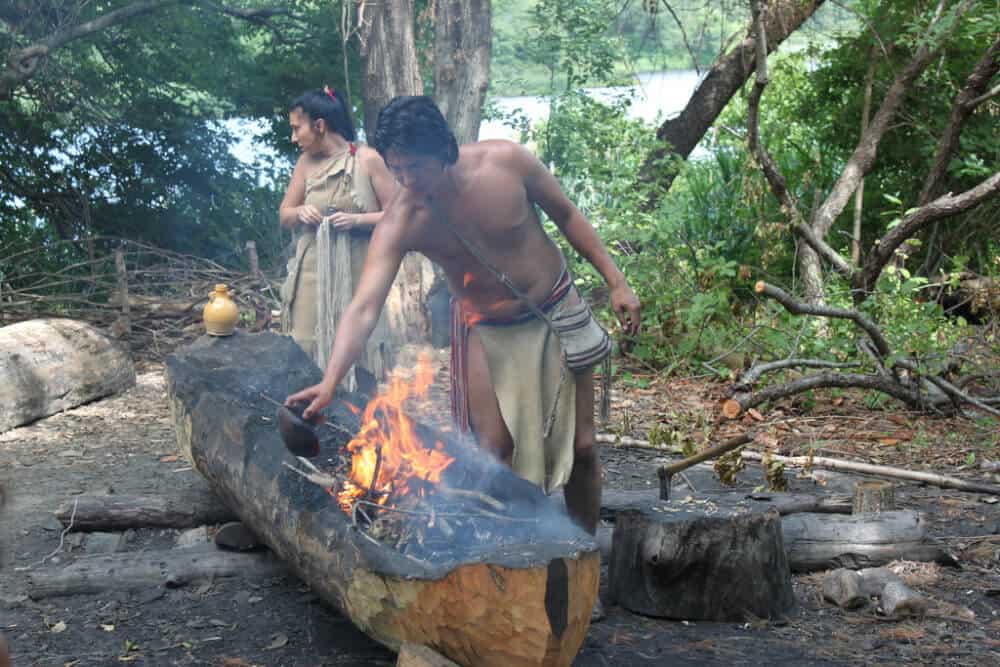 Two Wampanoag tribes people showing visitors how to make a traditional dugout canoe.