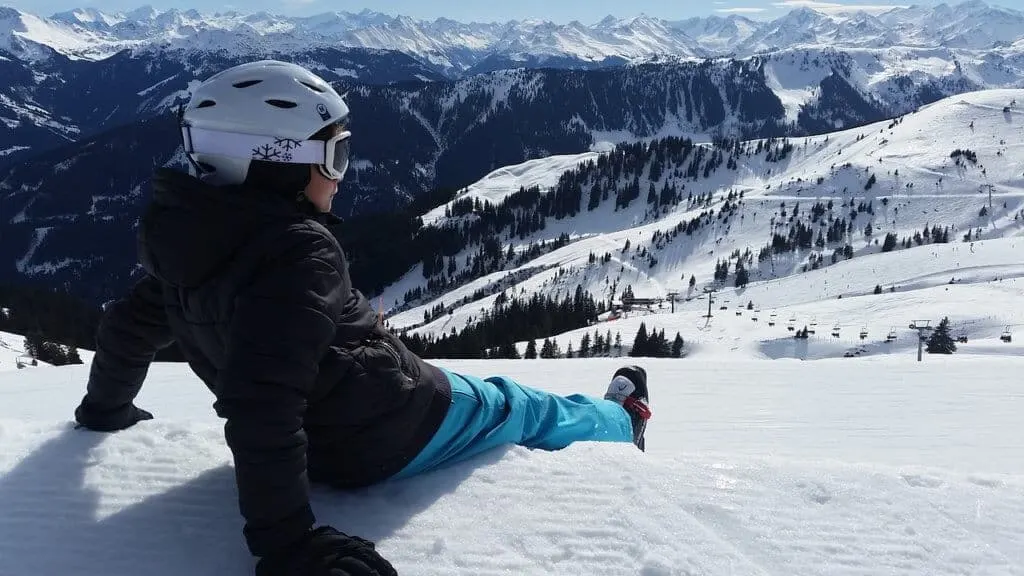 A young child sits on top of a mountain wearing ski clothing and gear. 