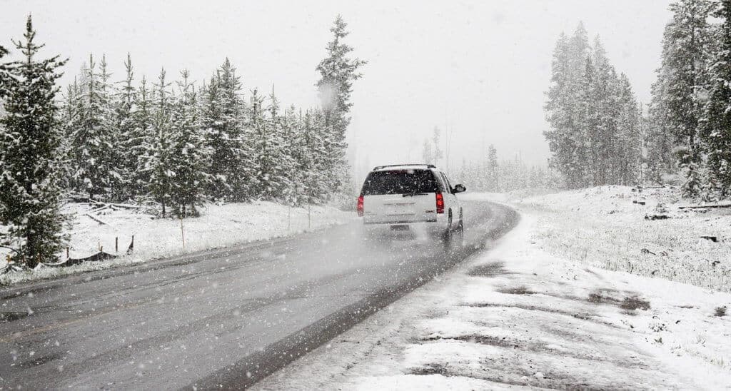 A white SUV drives along a snowy road on a winter road trip.