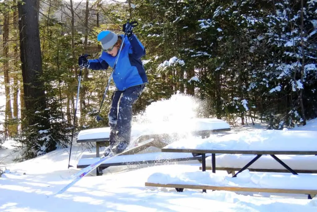 A skiier jumping of a picnic table covered with snow in Woodford State Park