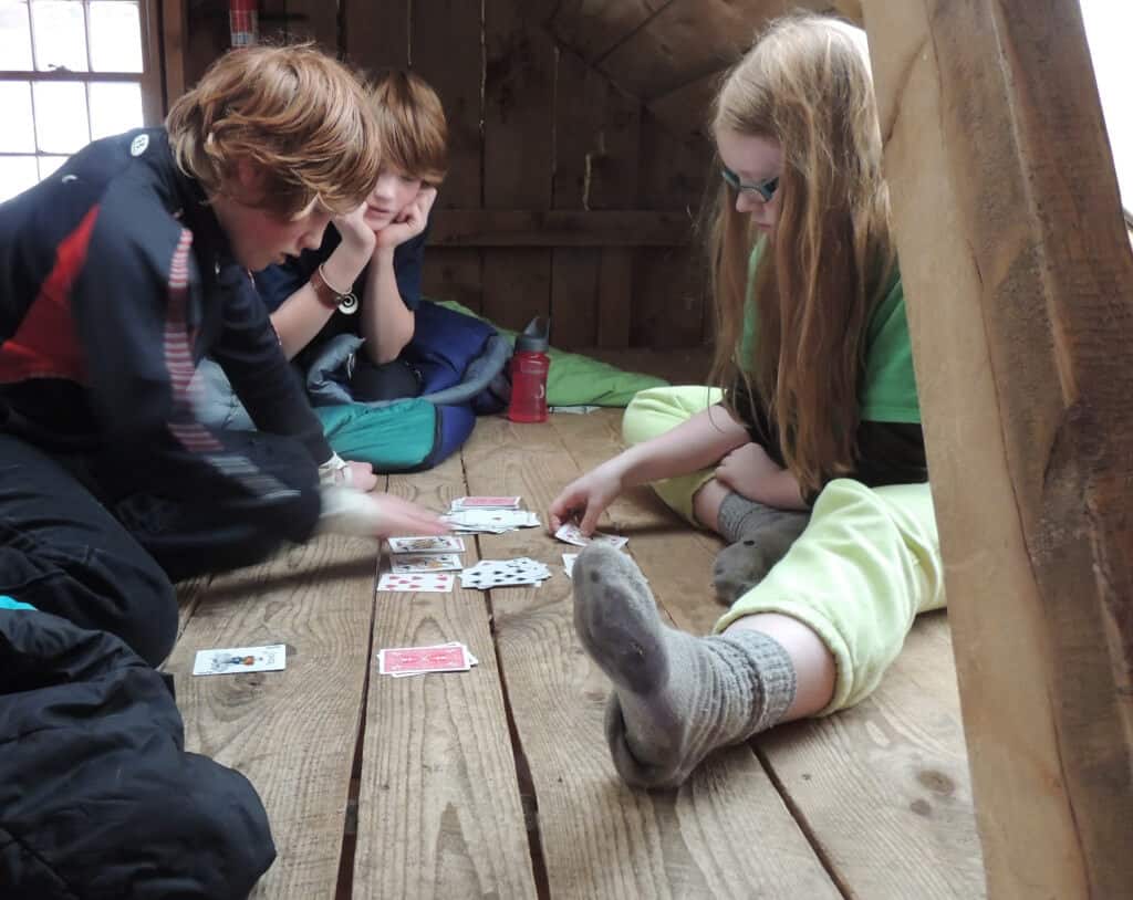 three kids playing cards on a wood floor