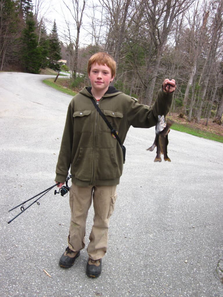 A boy holding up several small trout and a fishing pole