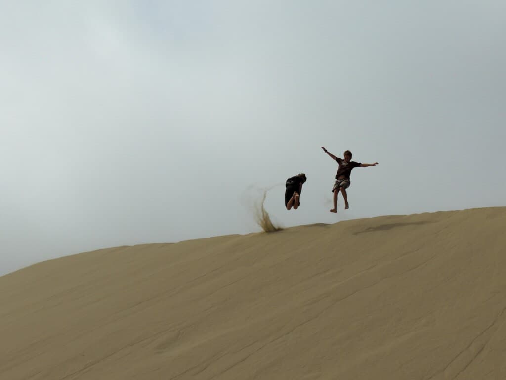 Two kids jumping in the sand at Oregon Sand Dunes
