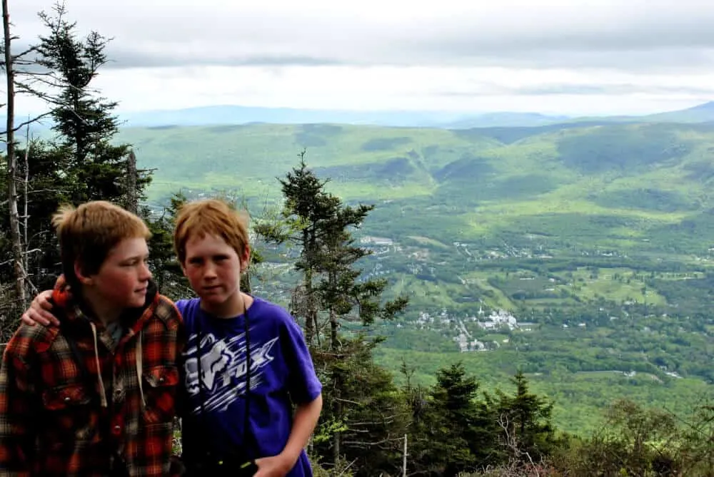 Two kids sit in front of a mountain vista in Vermont on a cloudy day.