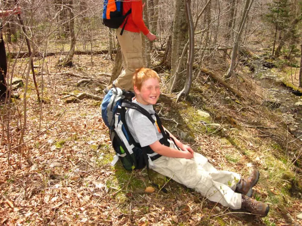 Gabriel sits on the ground wearing a backpack during a hike around Woodford State Park in Vermont.