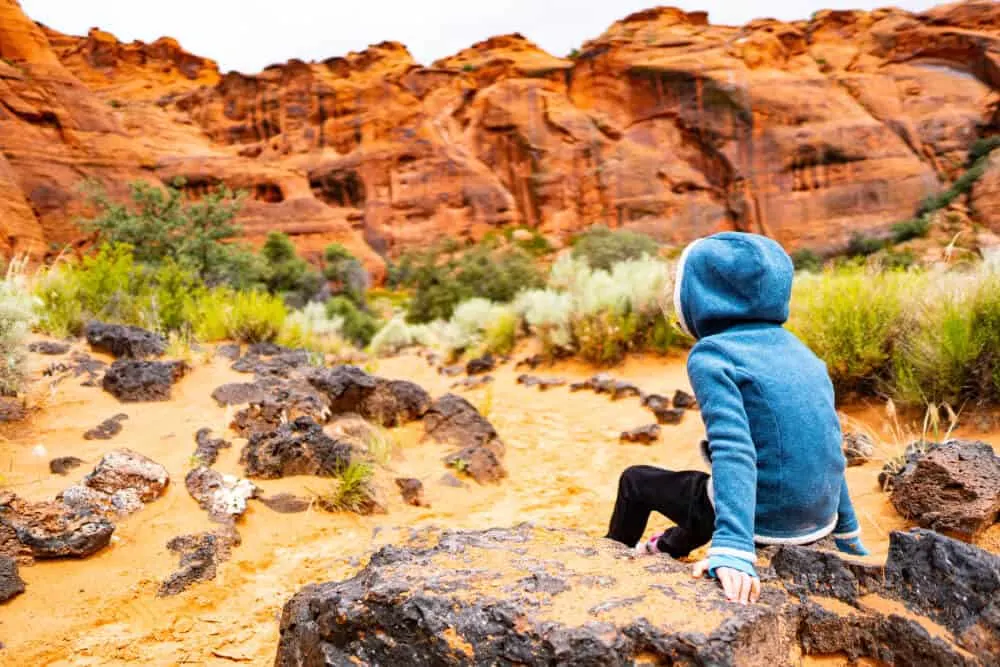 a child sits on a rock and looks out toward some red rocks in the background