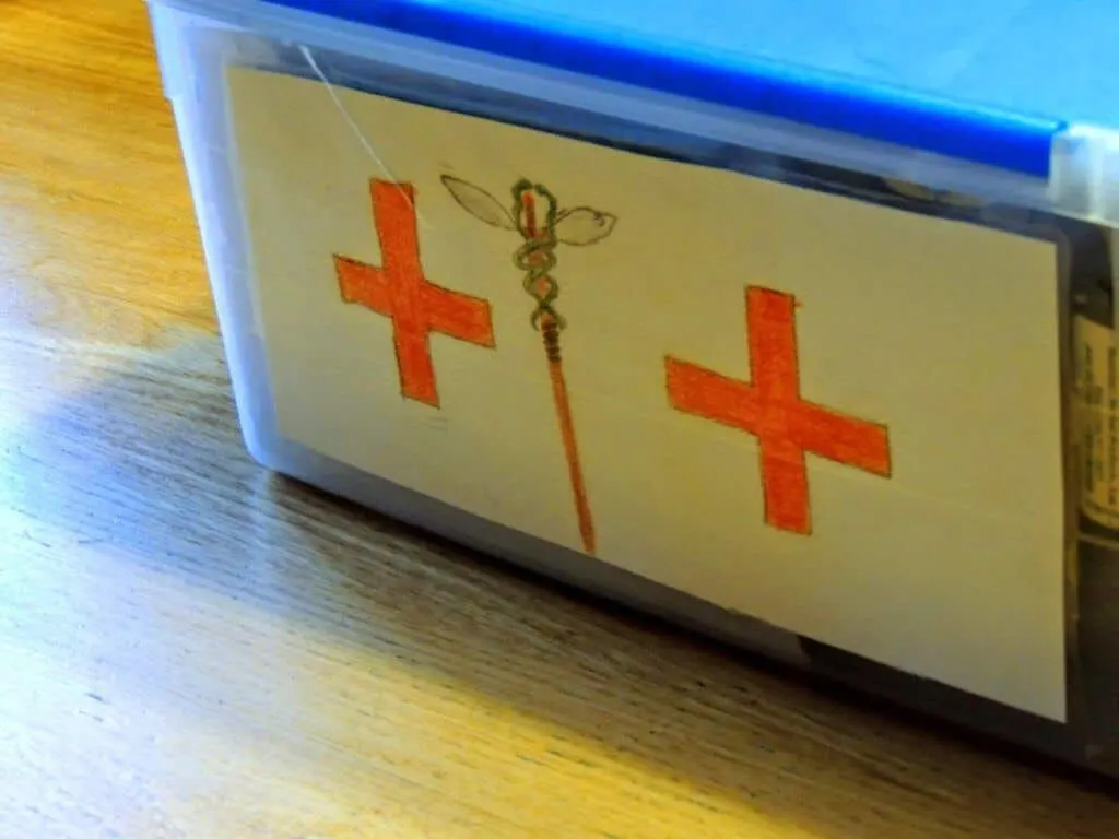 A plastic container with a drawing of a medical cross on it for a DIY travel first aid kit.