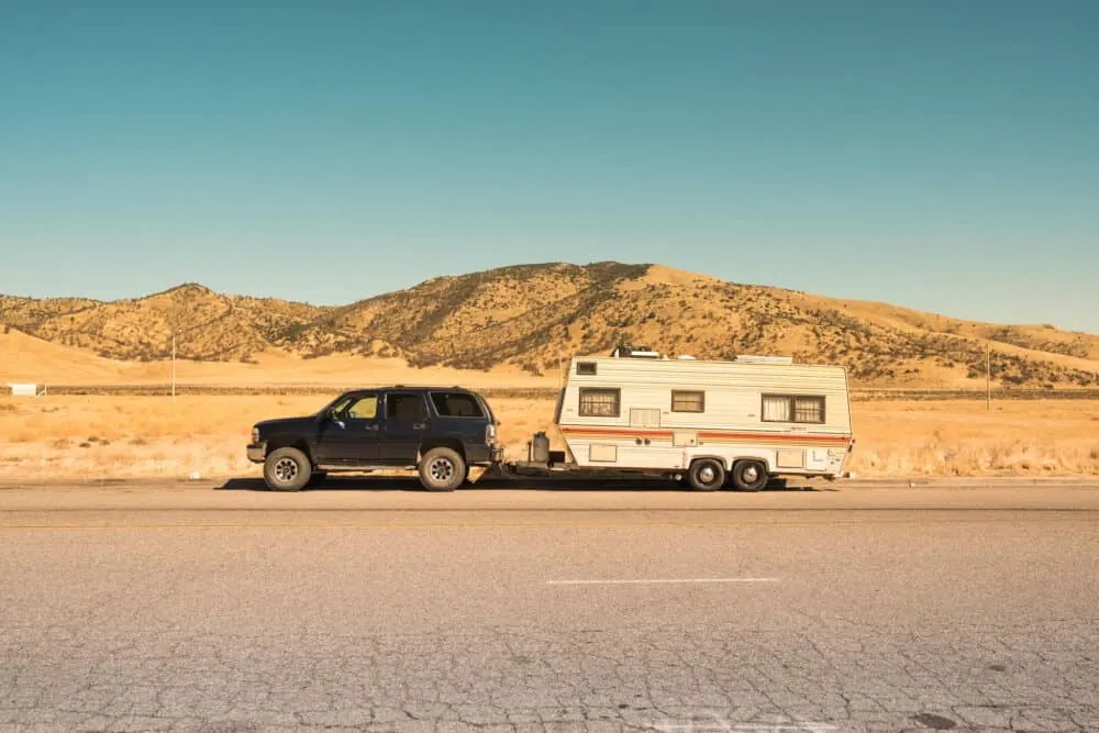 An SUV pulling an older camper through the desert.