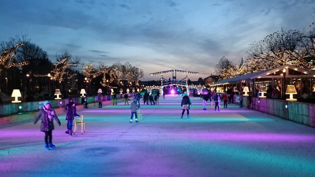 A night scene at an ice skating rink with many skaters and colorful lights. 