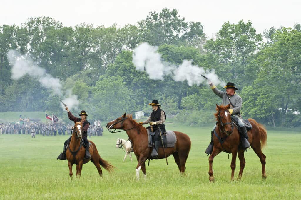Three men is Civil War dress ride horses during a reenactment