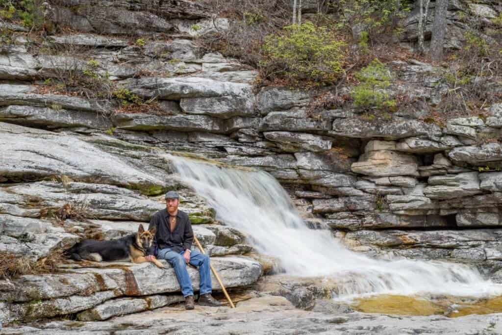 A man and a German Shepherd dog sitting next to a waterfall in the Hudson Valley New York