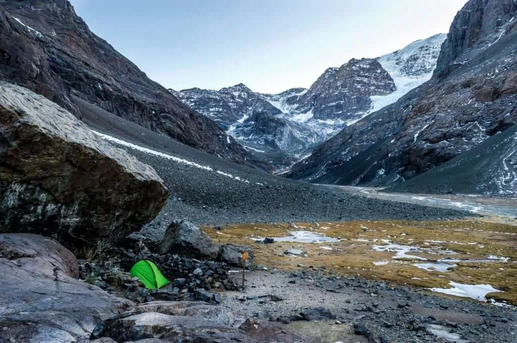 A green tent nestled into a hillside among snowcapped peaks during a spring camping trip.