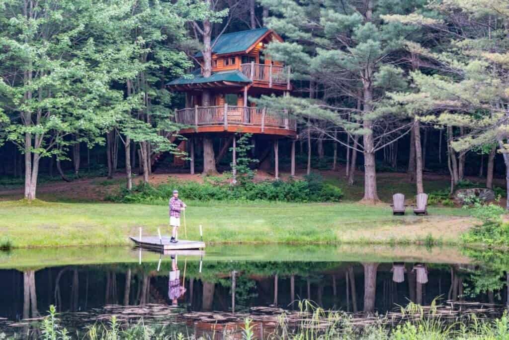 A man stands on a dock in front of a two-story treehouse in Vermont.