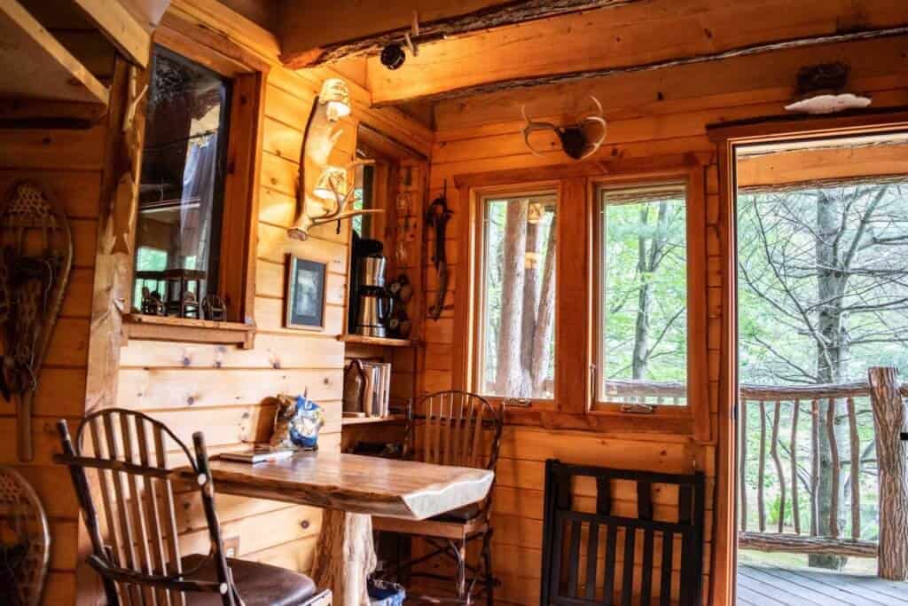 An inside view of our Vermont treehouse rental, with a small table and chairs, a coffee maker, and a picture window.