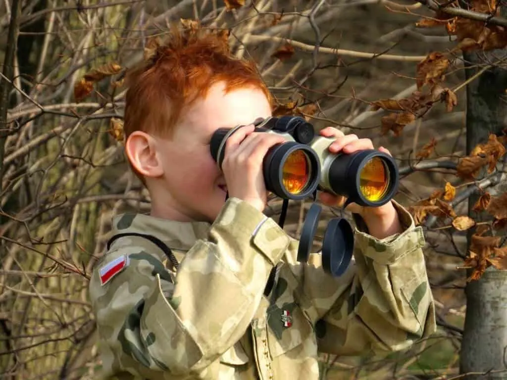 A young child holds binoculars up to his eyes to watch the birds.