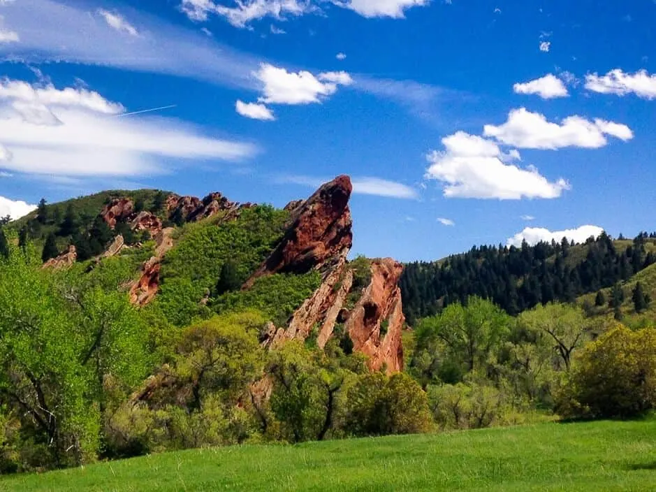 A nature scene - Red rocks jutting toward a blue sky, with green trees and grass all around. 