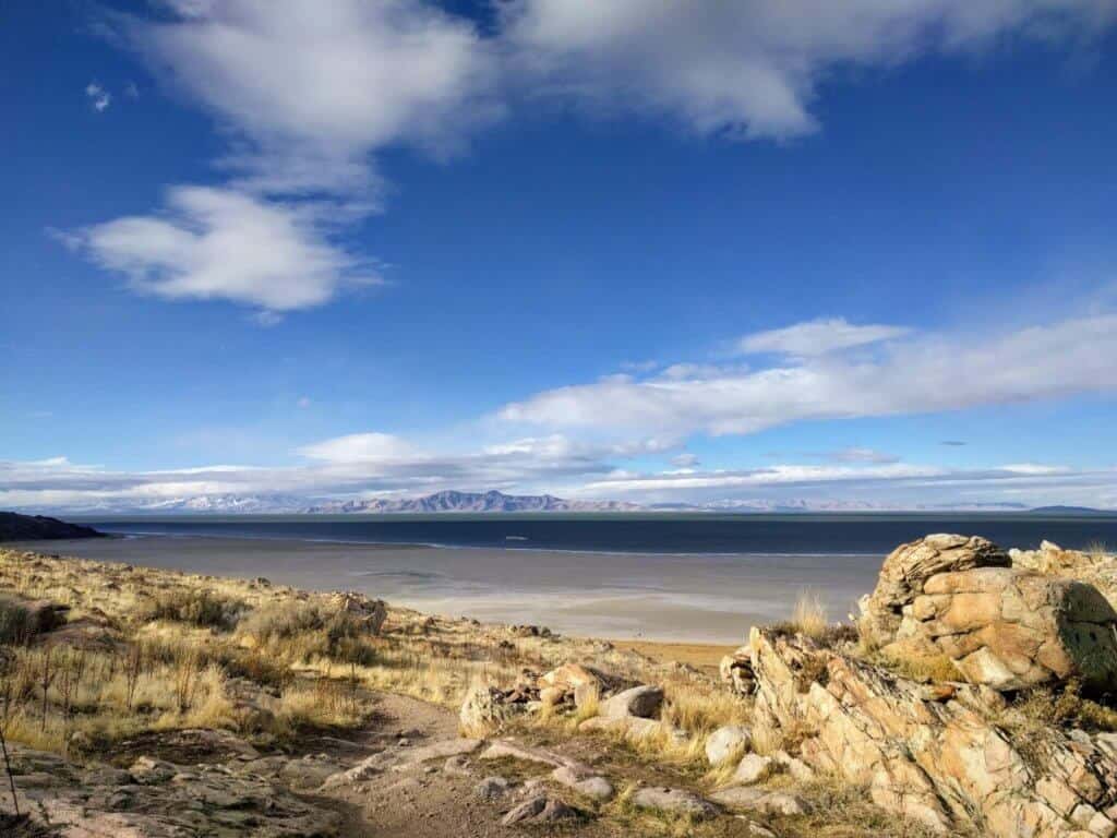 A scene of Antelope Island State Park in Utah - yellow rocks leading to the Great Salt Lake, with distant mountains and a clear blue sky.