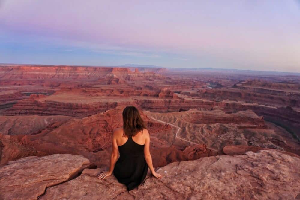 A back view of a seated woman looking out over the red rocks of Dead Horse Point State Park in UT