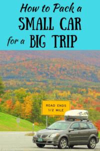 a shot of a small grey car in front of a hill during fall foliage season in Vermont. There is a sign behind the car that says 