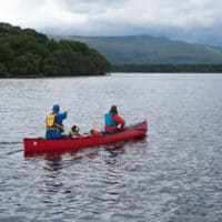 two people and a dog in a canoe on a mountain lake.