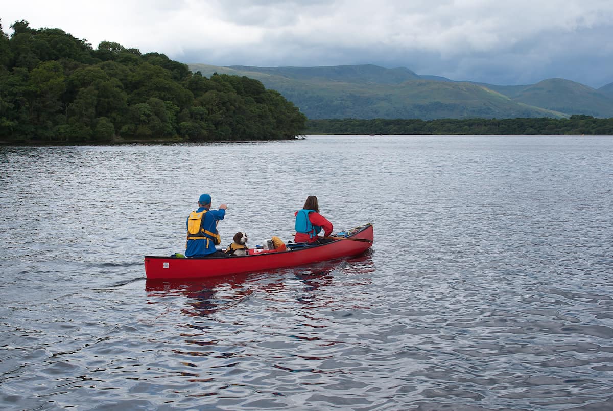two people and a dog in a canoe on a mountain lake.