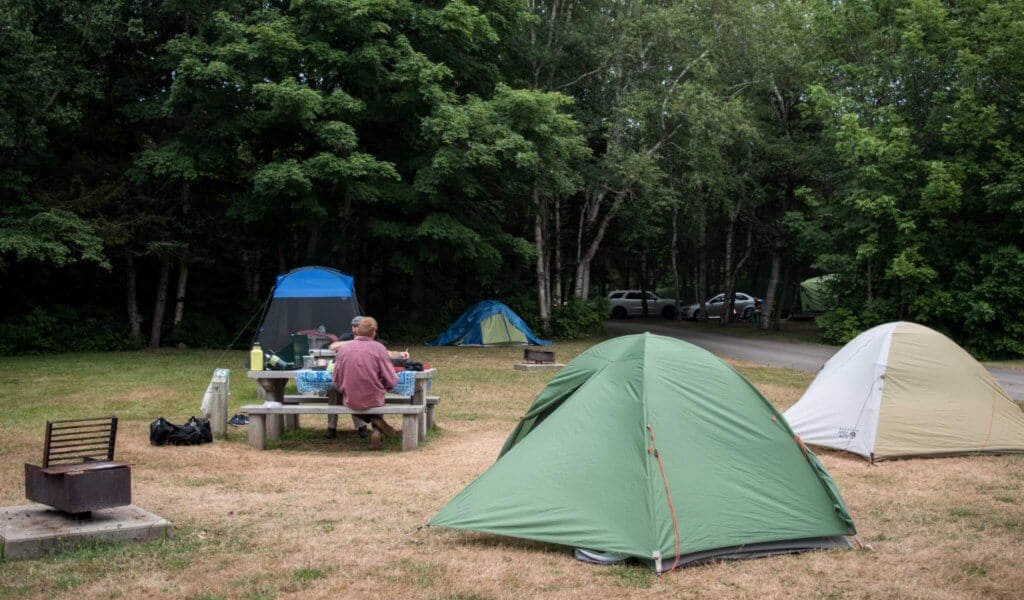 camping etiquette Two people sit at a picnic table surrounded by tents.