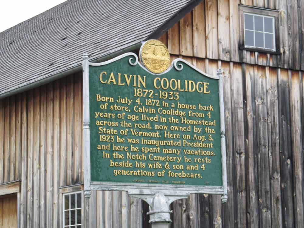 A sign at the Calvin Coolidge State Historic Site. It reads: Calvin Coolidge, 1872-1933. Born July 4, 1872 in a house back of store, Calvin Coolidge from four years of age lived in the Homestead across the road, now owned by the state of Vermont. Here on Aug. 3, 1923, he was inaugurated President and here he spent many vacations. In the Notch Cemetery he rests beside his wife & son and four generations of forebears. 