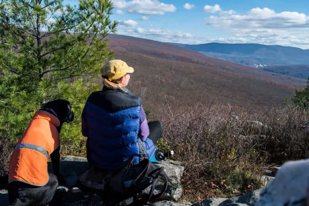 A woman sits next to a black dog at the top of Pine Cobble Mountain in Williamstown, Massachusetts.