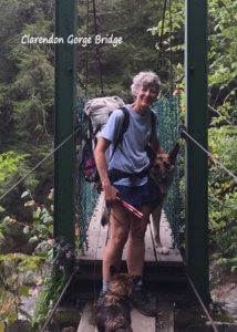 A woman stands on the Clarendon Gorge bridge. she is wearing a backpack and standing next to a German Shepherd.