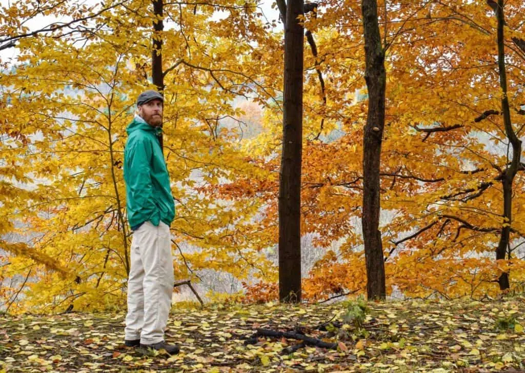a man stands in a forest full of colorful fall foliage.