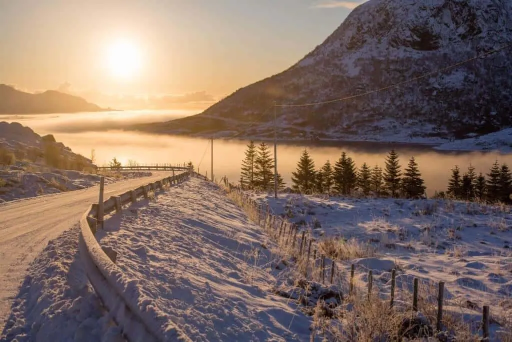 A snow covered road near a misty lake.