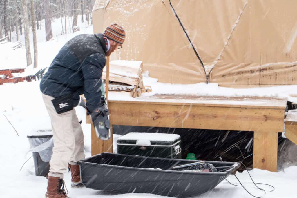 A man unloading a utility sled next to a camping shelter in Vermont.