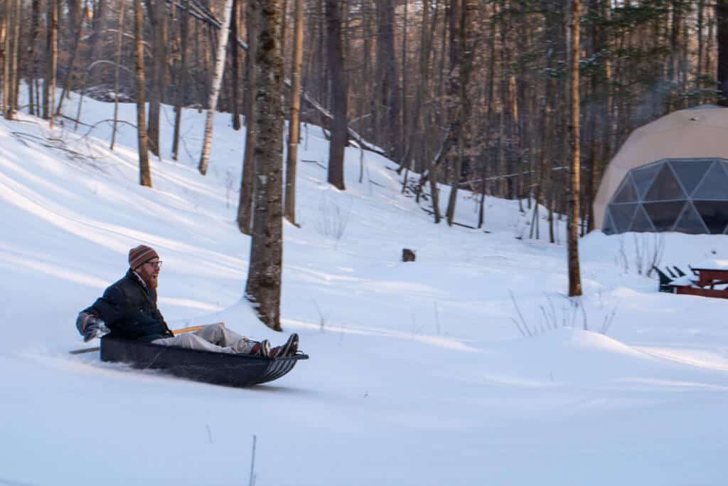 A man slides down a snowy hill in front of a geodesic dome in Vermont.