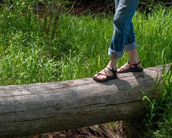 A pair of legs walks across a log wearing Chaco sandals.