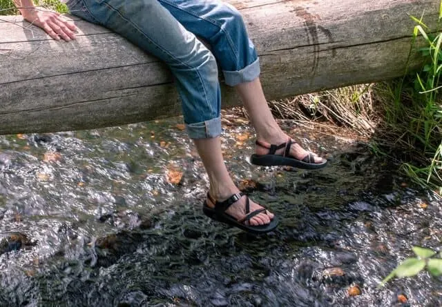 dangling feet above a stream. The feet are wearing Chaco sandals.