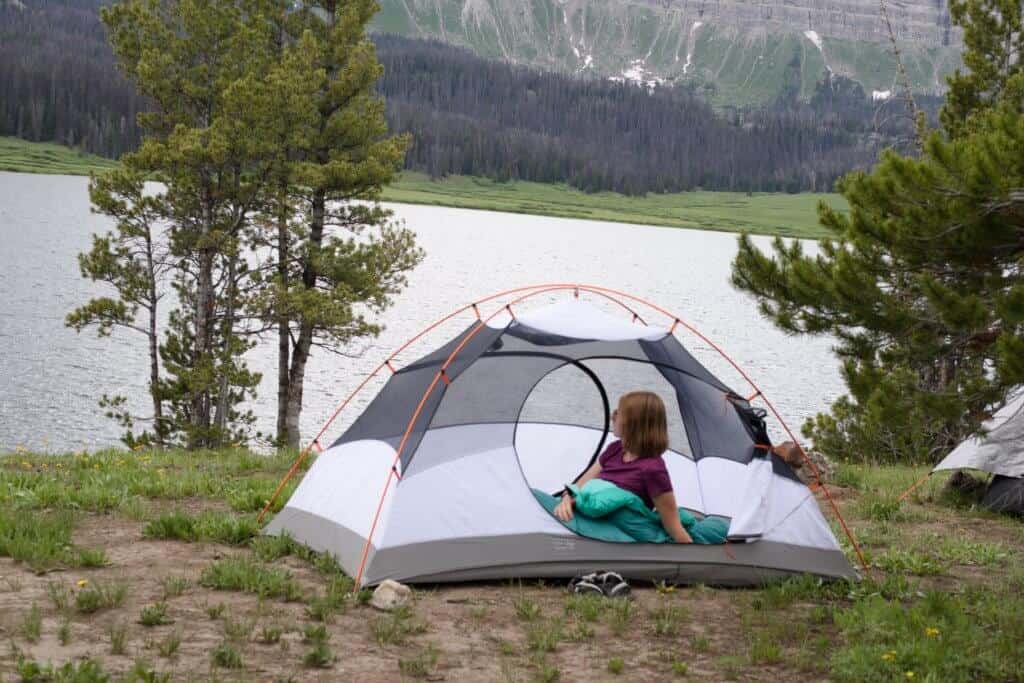 A woman lies in a two-person tent and checks out the beautiful view of the surrounding mountains.