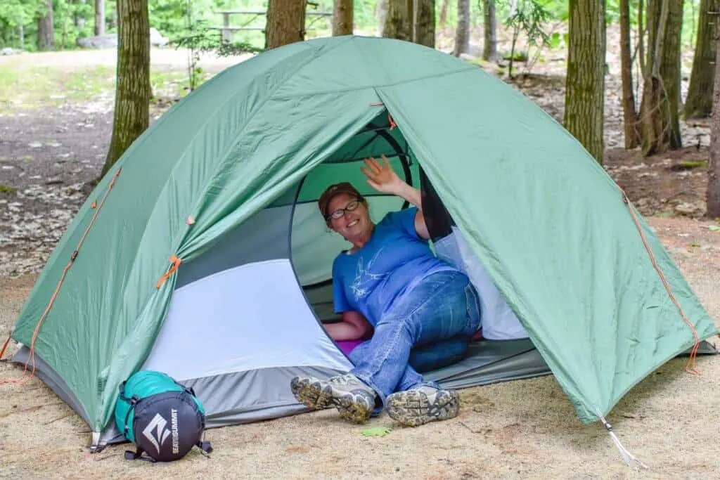 A woman lies inside of a tent smiling at the camera. 