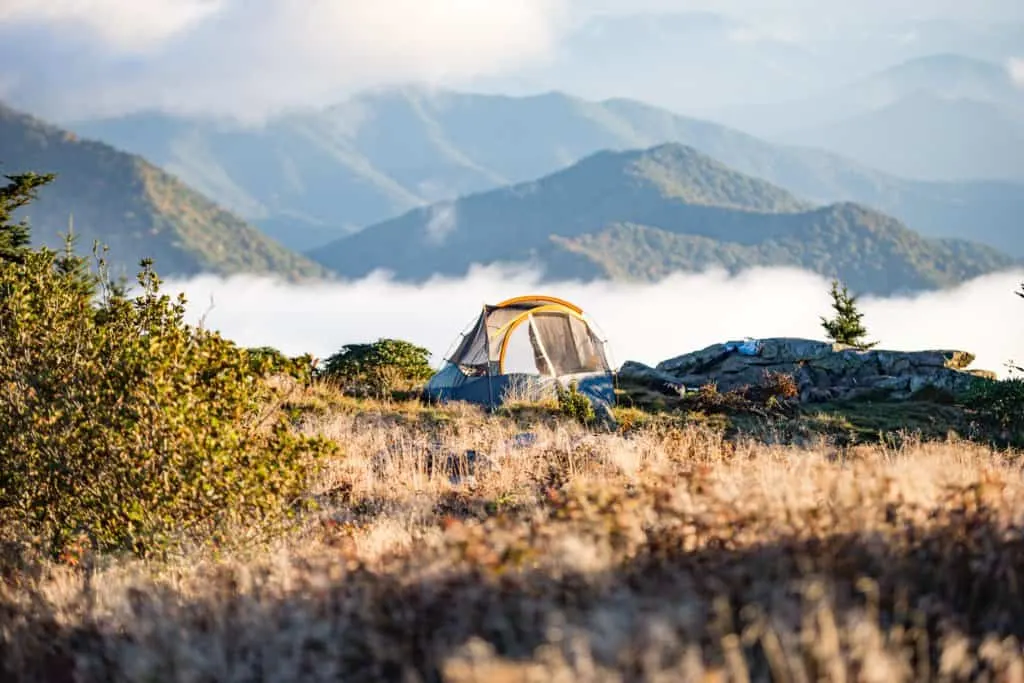 a tent in a field surrounded by mountains and fog.