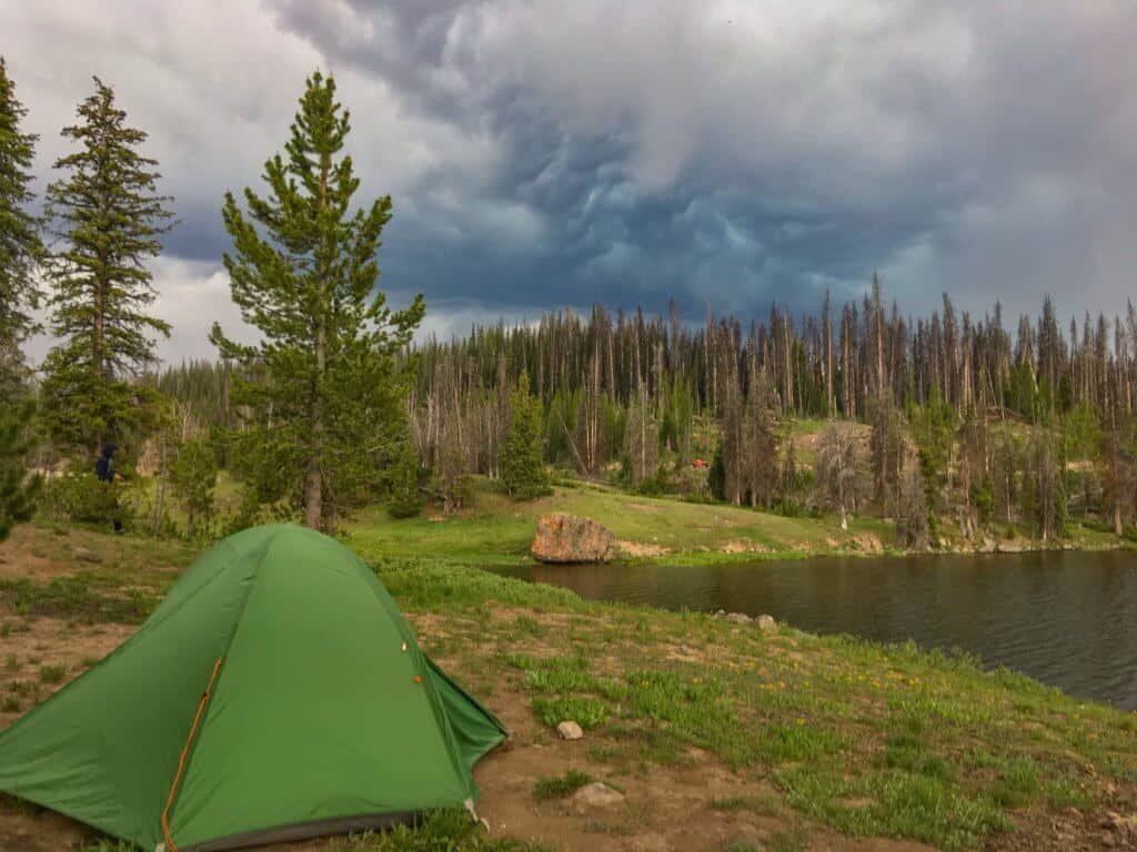 a green tent next to a small mountain lake in Wyoming.