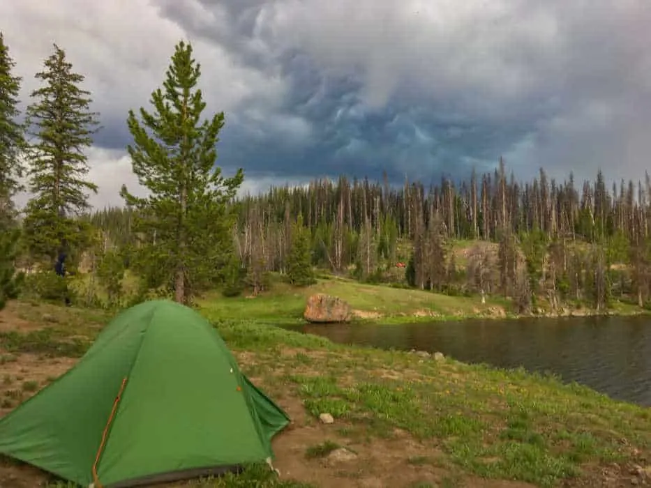 a green tent next to a small mountain lake in Wyoming.