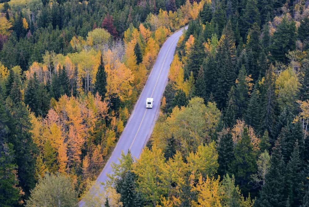 An RV drives on a quiet road through stunning fall foliage.