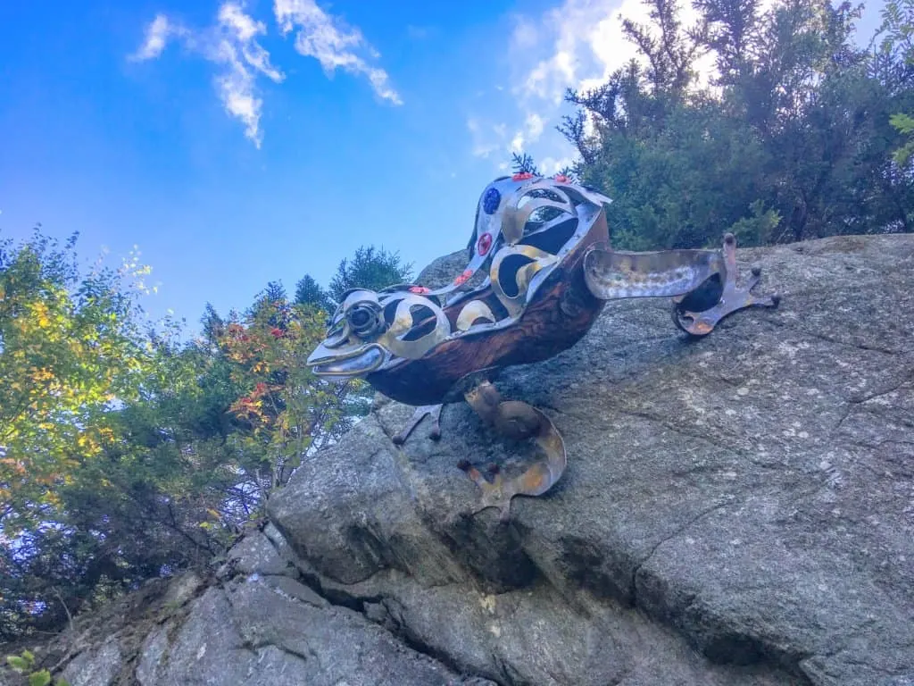 A giant metal and wood sculpture of a tree frog, perched on a boulder at Mont Sutton in Quebec.