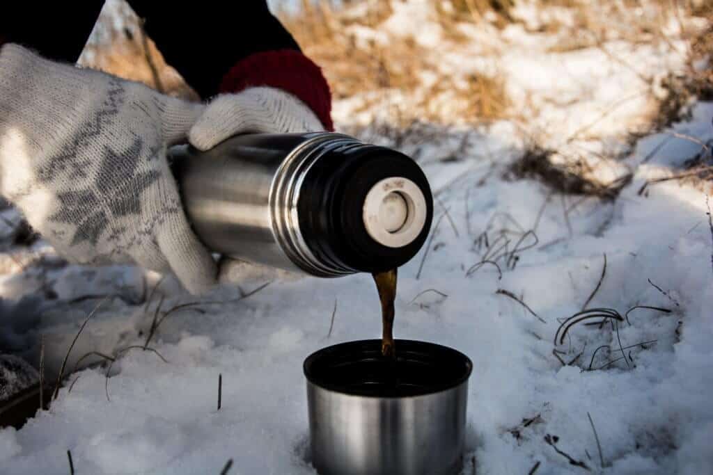 A pair of gloved hands pouring coffee from a thermos in the snow.