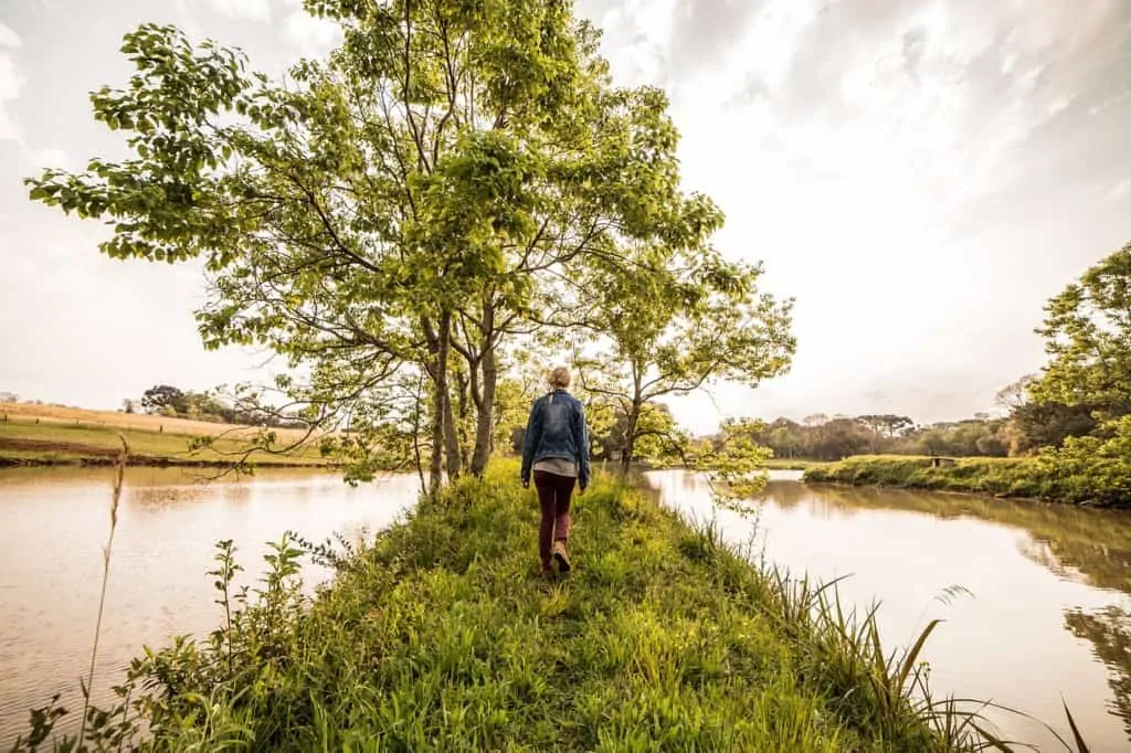 A woman walking on a narrow path of grass with water on both sides.