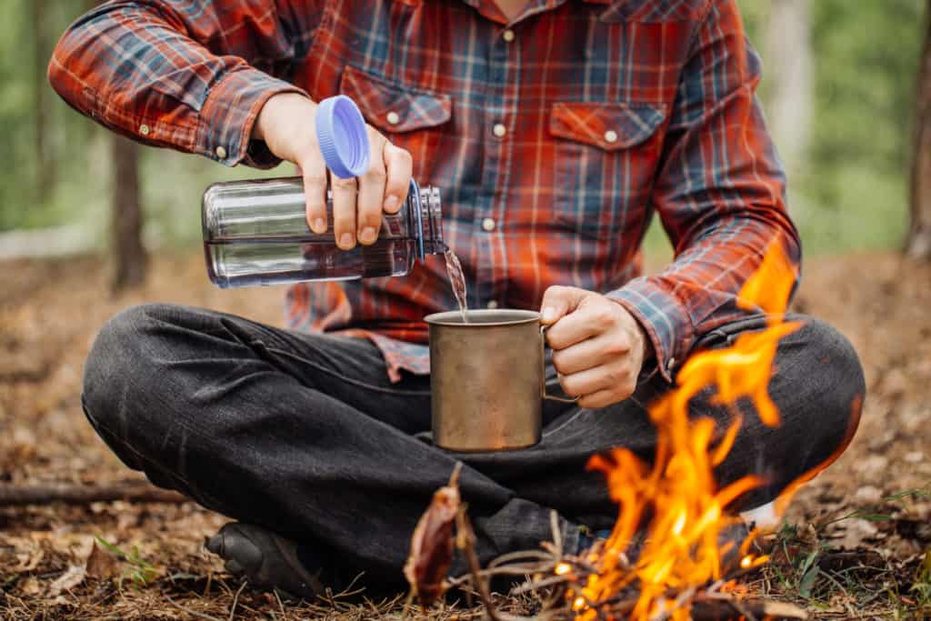 A man pours water into a camping mug.