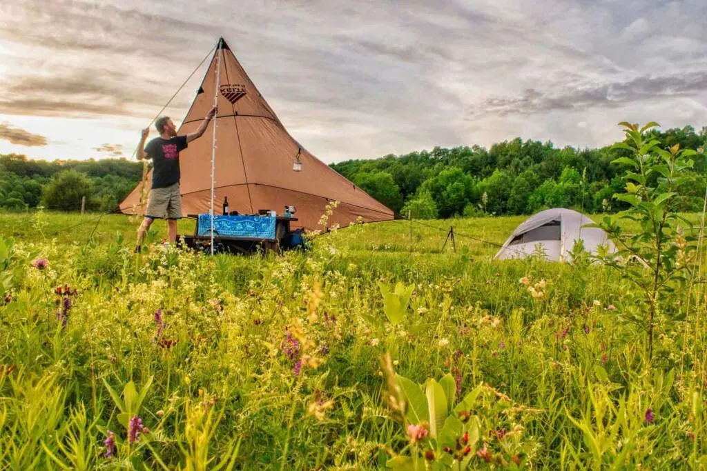 A man sets up a tarp over a picnic table at a campsite.