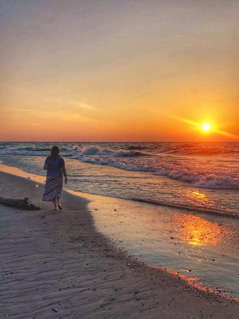 A woman walks along the shore at Indiana Dunes National Park at sunset.