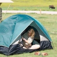 A woman sits in a tent in Badlands National Park with a bison in the background.