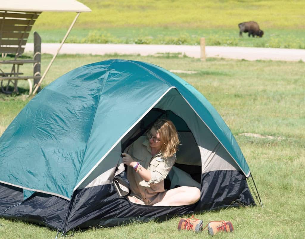 A woman sits in a tent in Badlands National Park with a bison in the background.