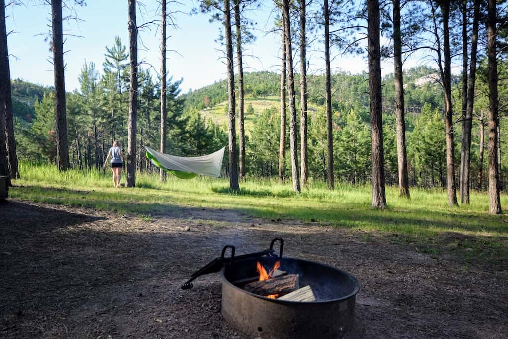 A firepit burning in Blue Bell Campground Custer State Park with a hammock in the distance.